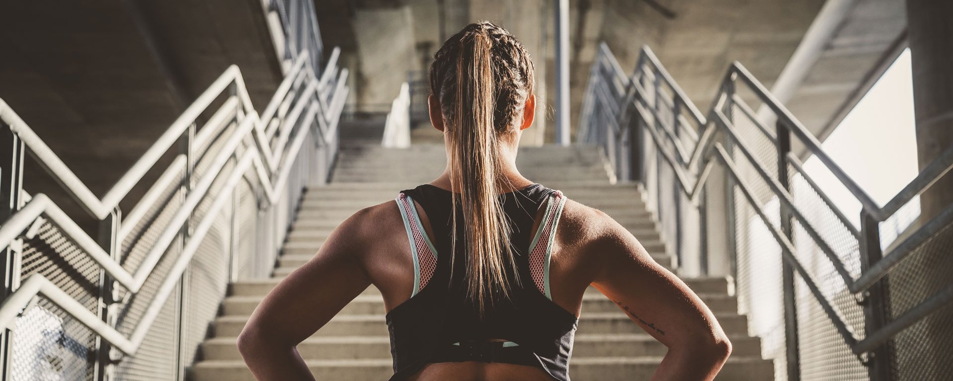 Eine Frau steht im Sportoutfit vor einer Treppe und ist bereits für neue Trainingsherausforderungen