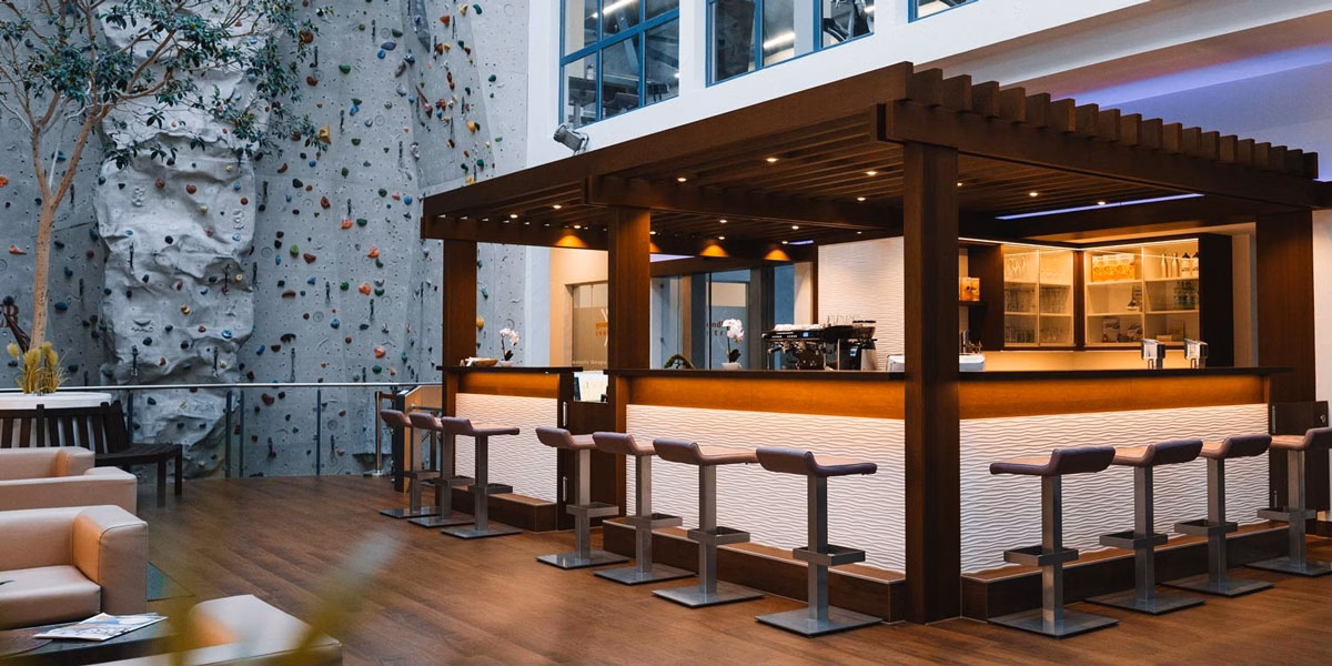 Moderner Cafébereich bei f+p Parks Waltenhofen mit Bar, Sitzplätzen und hoher Kletterwand im Hintergrund